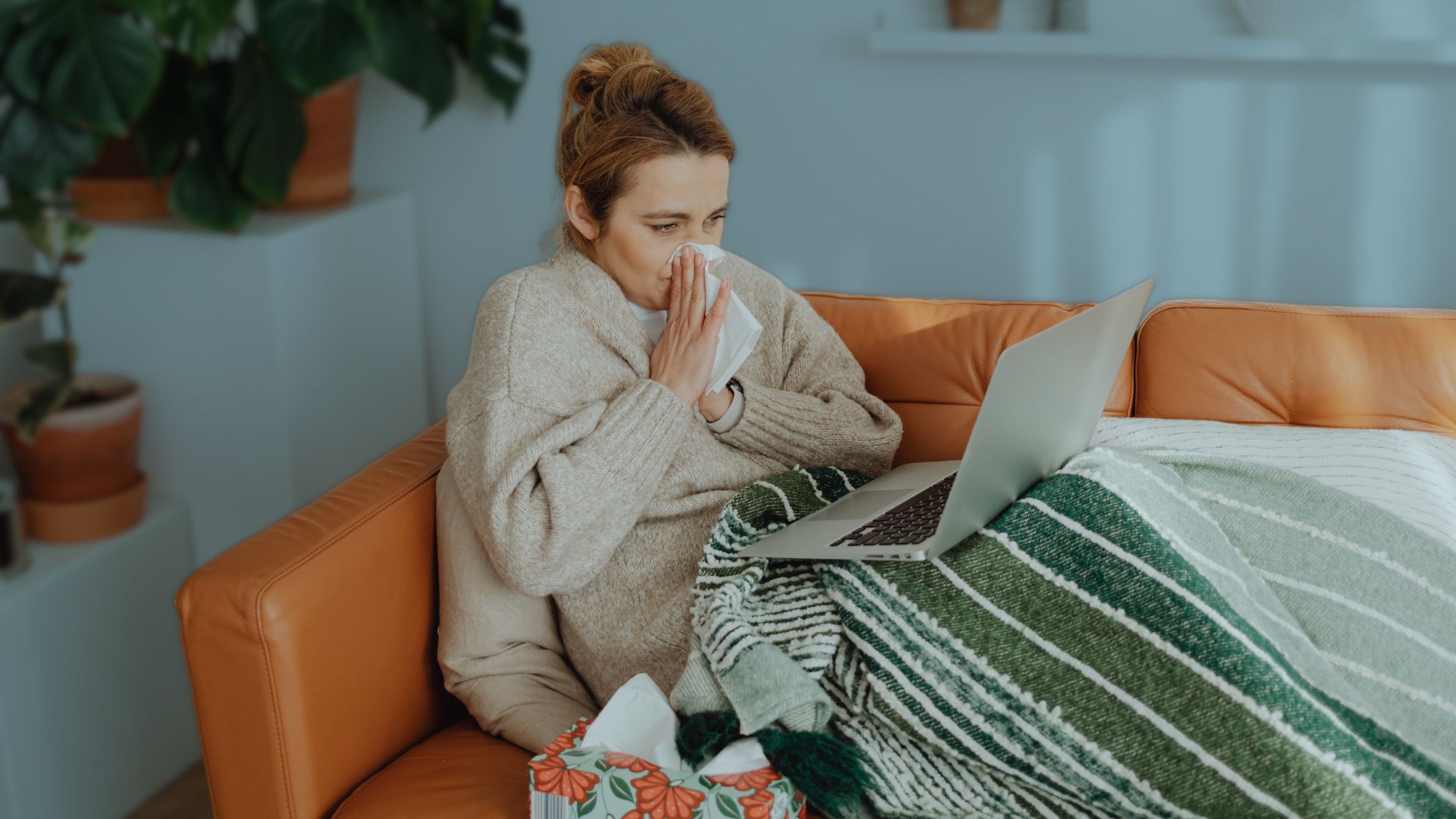 Woman Wiping Her Nose While Using a Laptop on Sofa